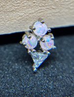 Close-up of a silver earring with three round opal-like stones and a single triangular clear gemstone set in prongs.