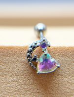 Close-up of a silver curved stud earring with a heart-shaped iridescent purple gemstone set against textured skin.