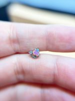 A tiny iridescent heart-shaped gem held between fingers