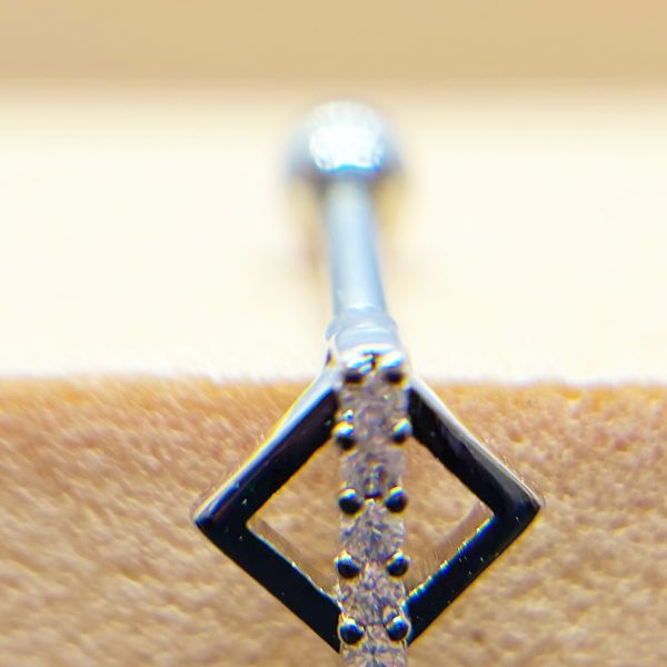 Close-up of a small diamond-studded pendant with a square frame and vertical row of tiny stones on a textured background