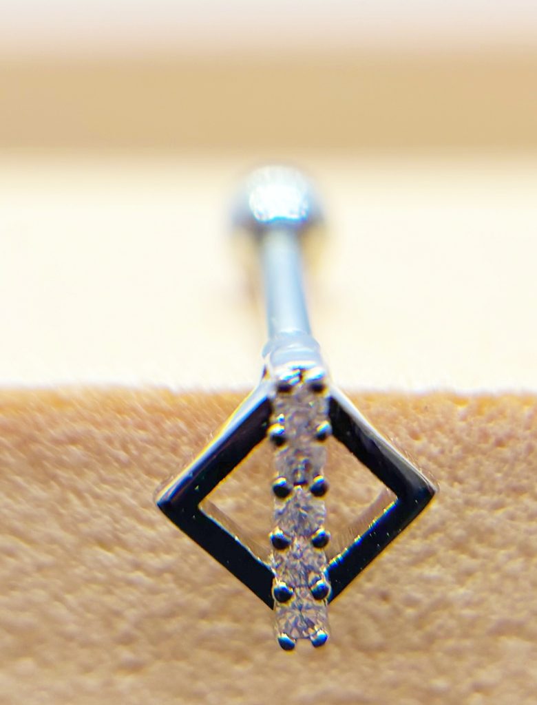 Close-up of a small diamond-studded pendant with a square frame and vertical row of tiny stones on a textured background