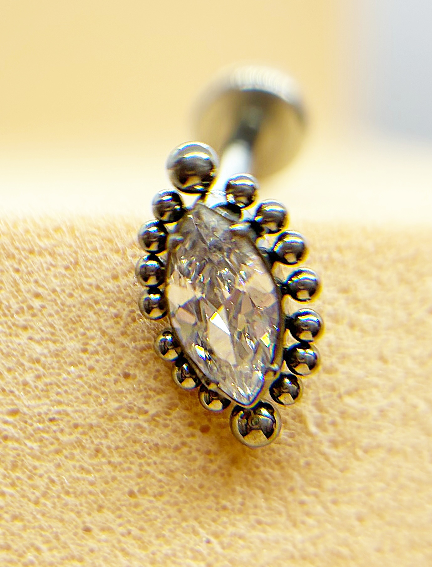Close-up of a silver earring with a marquise-cut clear stone and bead-like settings on a warm background