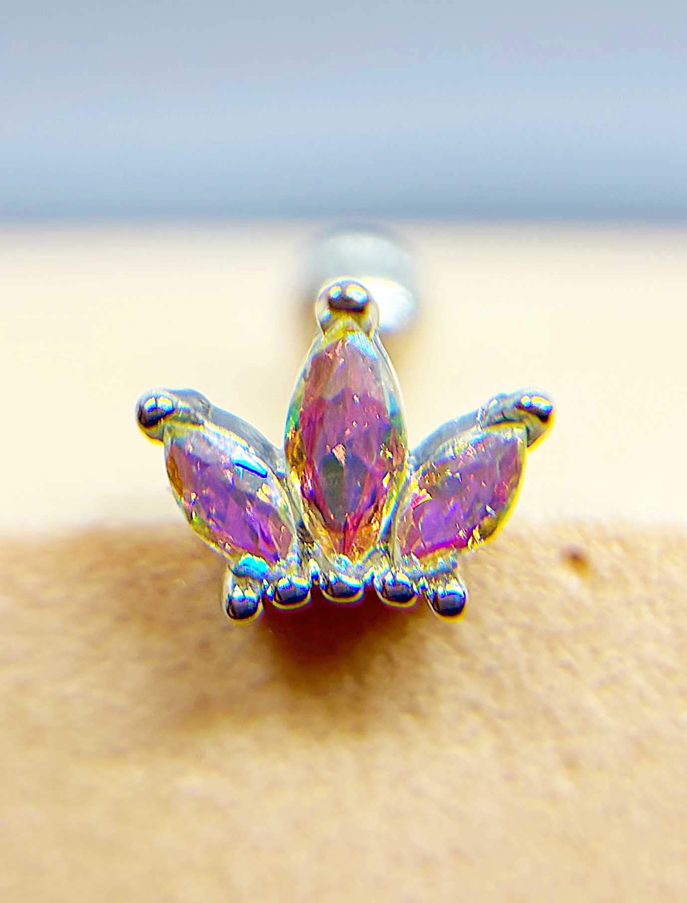 Colourful jeweled nose stud with three purple teardrop stones in a gold setting attached to skin