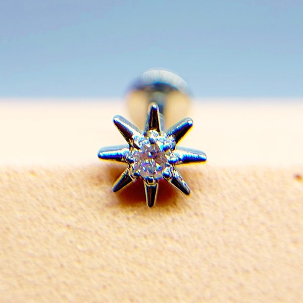 Close-up of a metallic star-shaped stud earring on a beige surface, with a blurred background