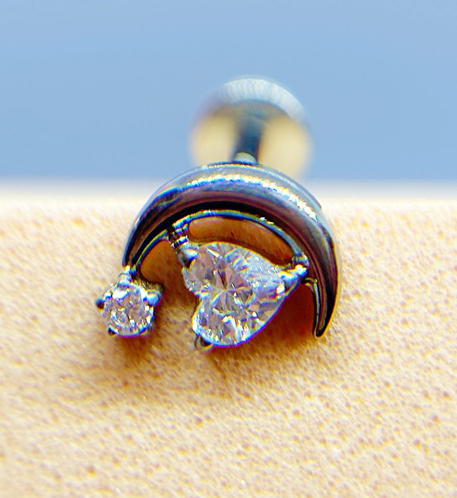 Close-up of a curved ear stud with two clear gemstones on skin, against a blue background