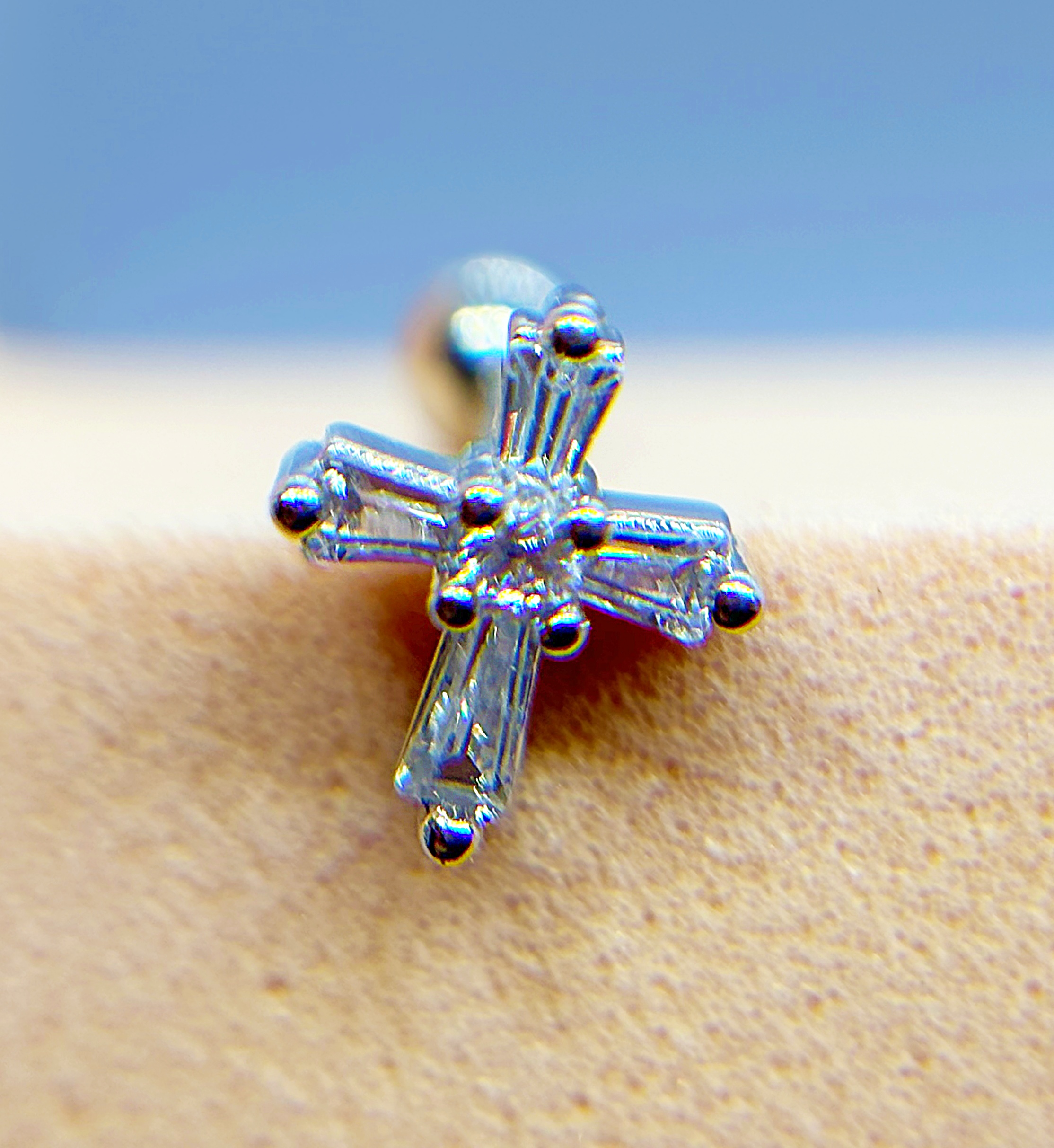 Close-up of a silver cross-shaped crystal earring against skin with a blue background