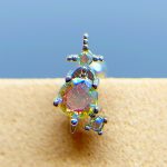 Close-up of an iridescent gemstone stud earring with a dangling accent on skin, against a blue background