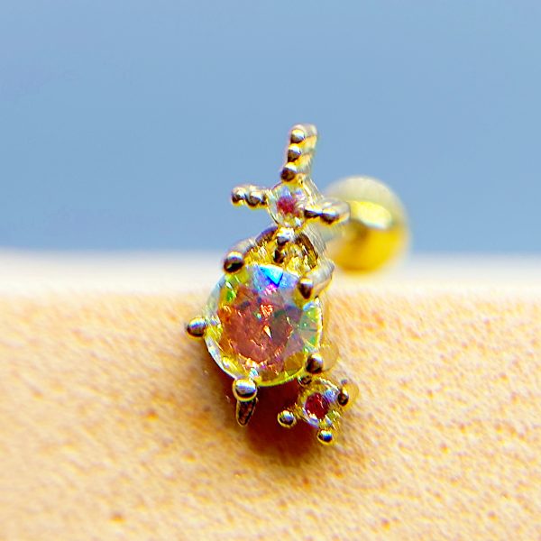 Close-up of a colourful gemstone ring on skin, with a blurred gold stud earring in the background