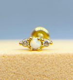 Close-up of a gold nose stud with a white centre gem and small clear stones on a blue background