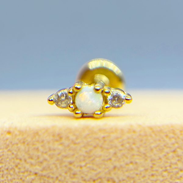 Close-up of a gold nose stud with a white centre gem and small clear stones on a blue background