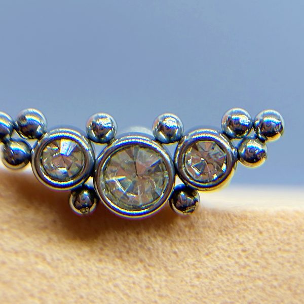 Close-up of a silver beaded nose stud with three clear gemstones on skin against a blue background