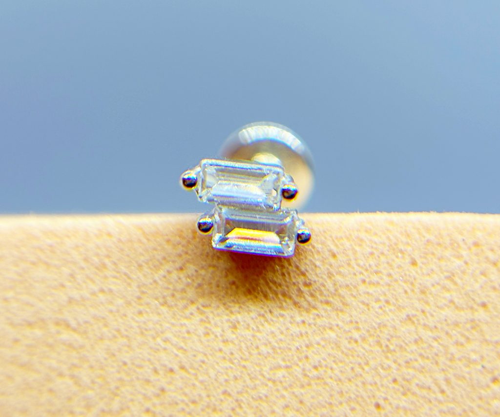 Close-up of a tiny clear gemstone earring on a warm-toned surface against a blue background