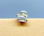 Close-up of a tiny clear gemstone earring on a warm-toned surface against a blue background
