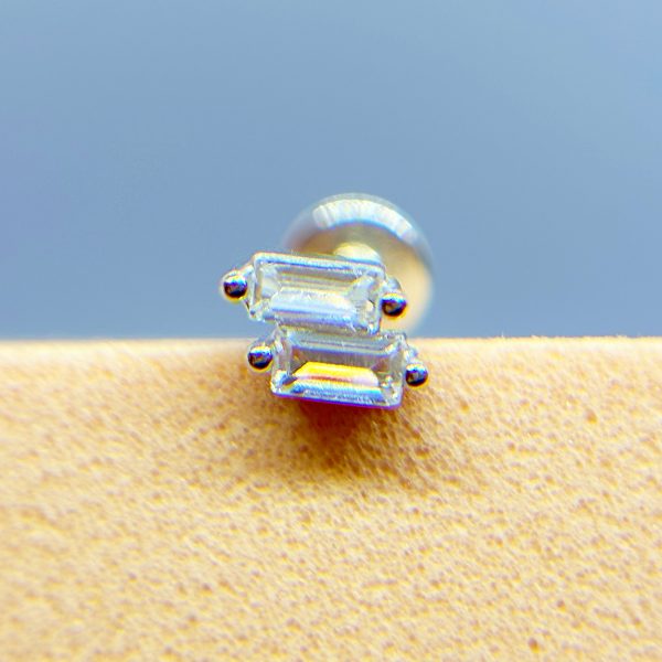 Close-up of a tiny clear gemstone earring on a warm-toned surface against a blue background