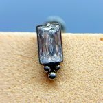 Close-up of a rectangular clear gemstone stud earring on skin, with a blue background