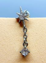 Close-up of a silver starburst earring with dangling chain and gem, worn on skin against a blue background