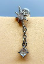 Close-up of a star-shaped gemstone stud earring with a dangling clear gem on skin