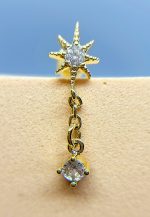 Gold star-shaped earring with clear gemstones and a dangling round crystal against skin