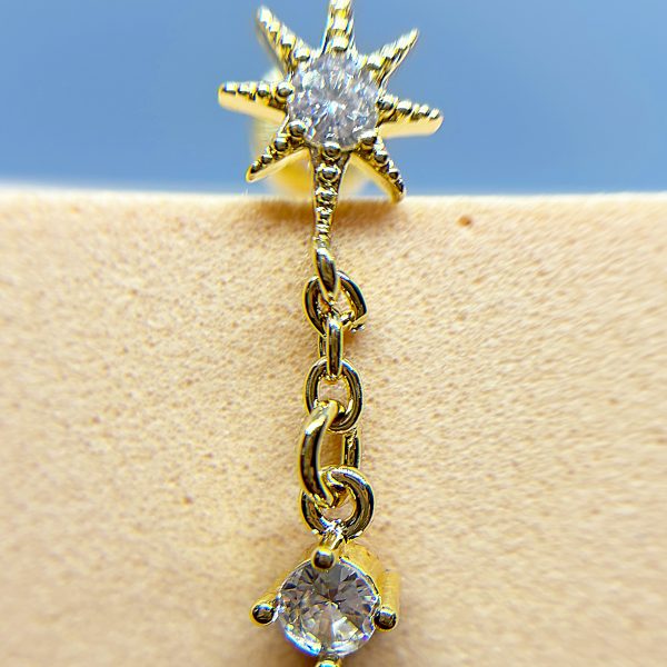 Gold star-shaped earring with clear gemstones and a dangling round crystal against skin