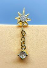 Close-up of a gold starburst earring with two clear gemstones on a blue and beige background