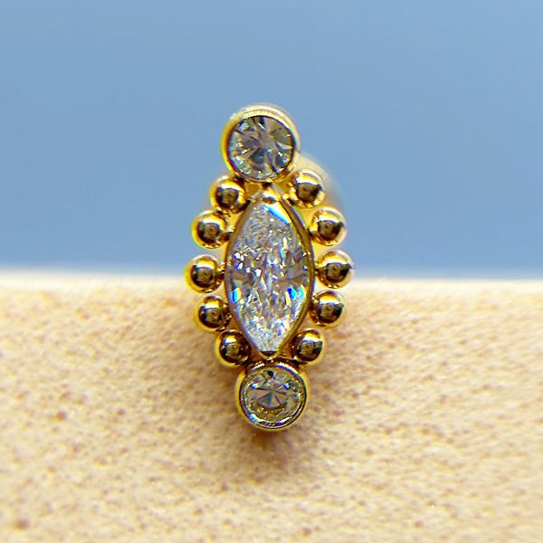 Close-up of a gold and clear gemstone stud earring against a blue and beige background