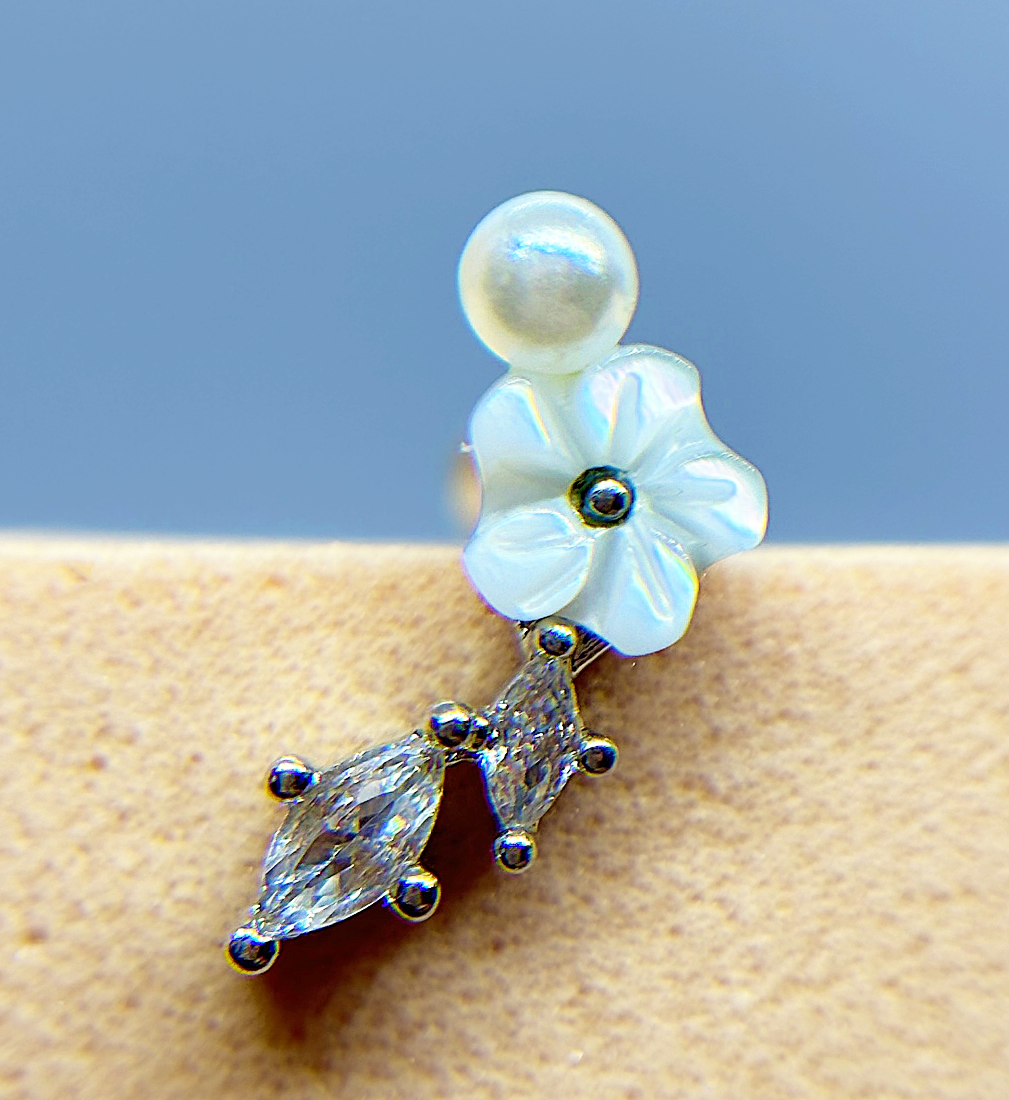 IMG_9336 Close-up of a pearl and crystal flower-shaped earring against a blue background