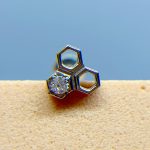Close-up of a silver hexagon-shaped earring with a small gemstone on a beige surface