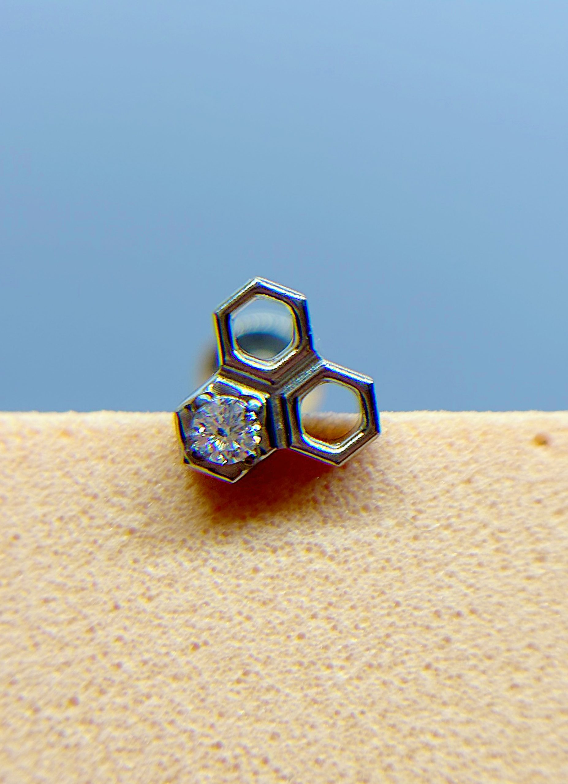 IMG_9338 Close-up of a silver hexagon-shaped earring with a small gemstone on a beige surface