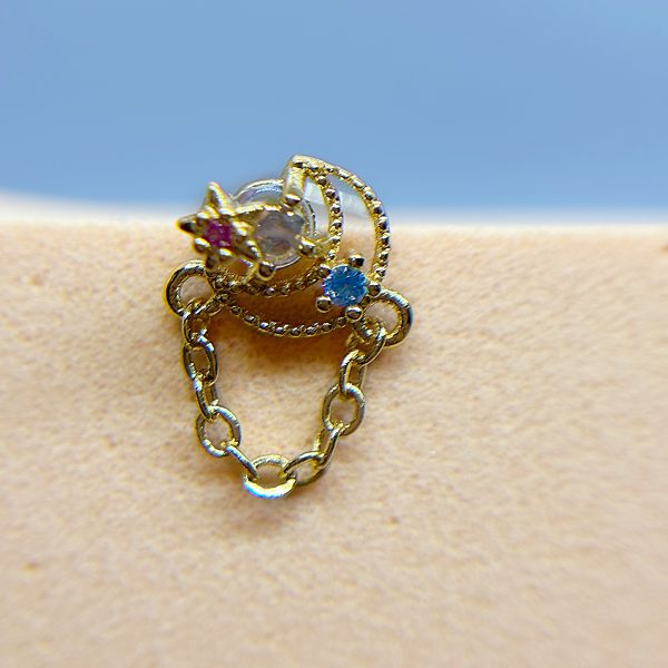 Gold nose stud with a dangling chain and small blue and red gems on skin