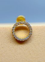 Close-up of a gold earring hoop set with small clear gemstones against a blurred blue and beige background