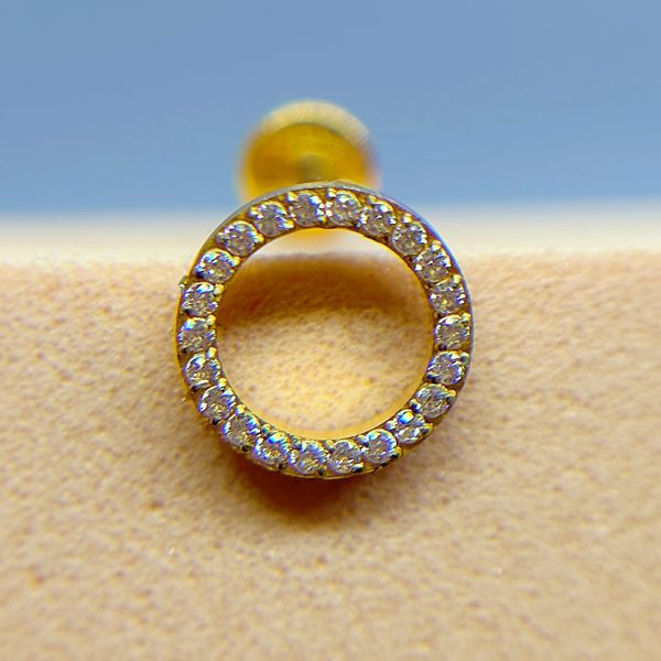 Close-up of a gold earring hoop set with small clear gemstones against a blurred blue and beige background