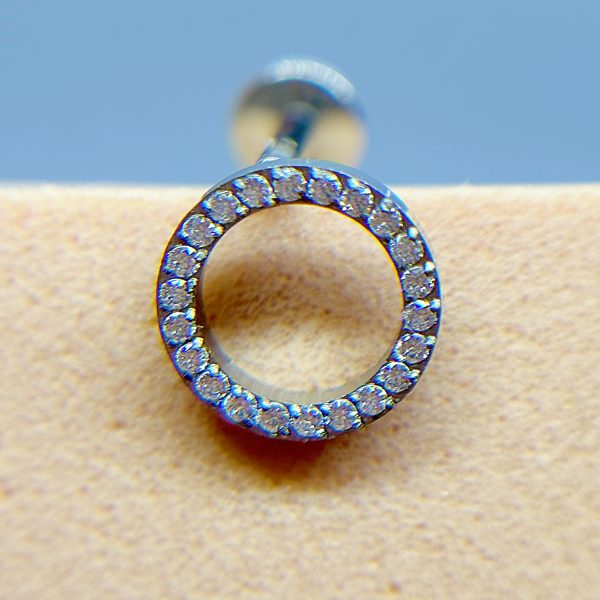 Diamond-studded circular ear stud on skin, shown in close-up