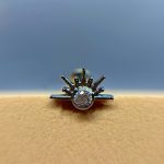Close-up of a silver sunburst ring with a large central diamond on a beige surface against a blue background