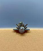 Close-up of a silver sunburst ring with a large central diamond on a beige surface against a blue background