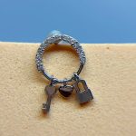 Silver hoop earring with key, heart and padlock charms on a skin-toned background