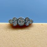 Close-up of a silver nose stud with clear gemstones against skin and a blue background
