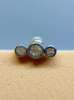 Three diamond studs arranged in a row on a beige surface, with a blue background
