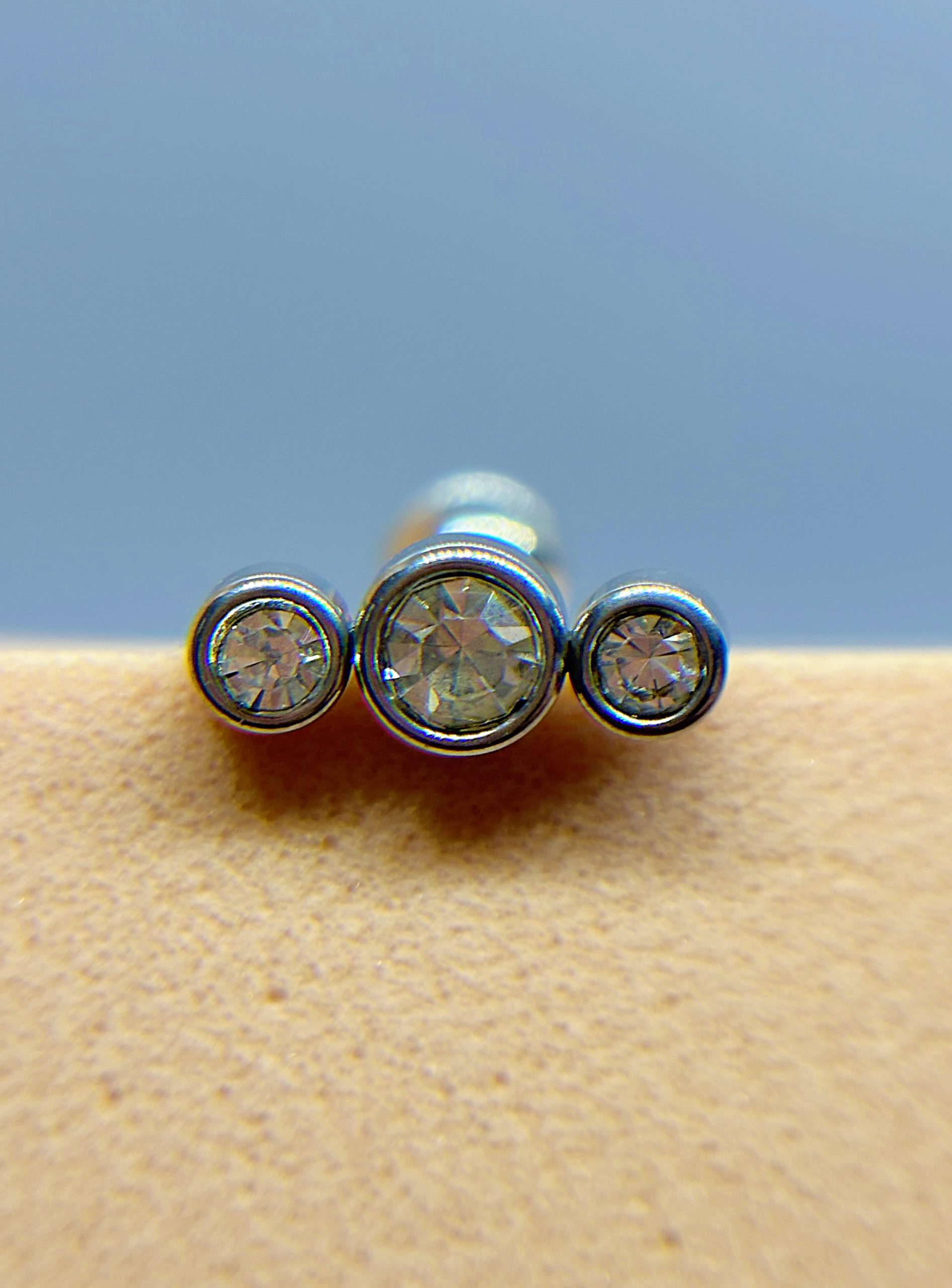 IMG_9362 Three diamond studs arranged in a row on a beige surface, with a blue background
