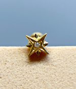 Gold star-shaped stud earring with a clear centre gem on a beige background