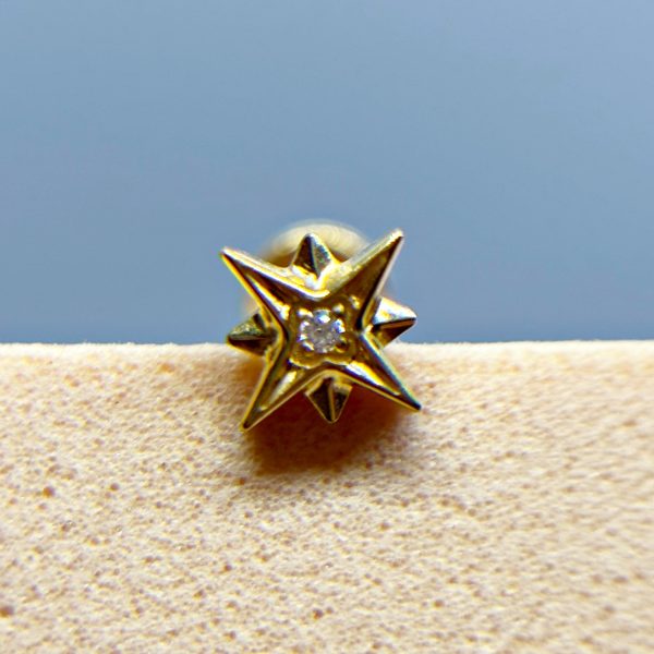 Gold star-shaped stud earring with a clear centre gem on a beige background