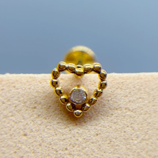 Close-up of a gold beaded earring with a central clear stone against a soft blue background