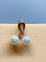 Close-up of a pearl drop earring with two white beads on a gold loop against beige skin and blue background