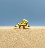 Macro of a tiny gold cactus-shaped stud earring on a beige surface against a blue background