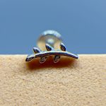 Close-up of a shiny metal object with three looped prongs against a blue background and textured beige surface
