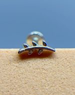 Close-up of a shiny metal object with three looped prongs against a blue background and textured beige surface