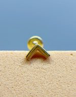 Close-up of a gold stud earring with a chevron-shaped front on a textured surface against a blue background