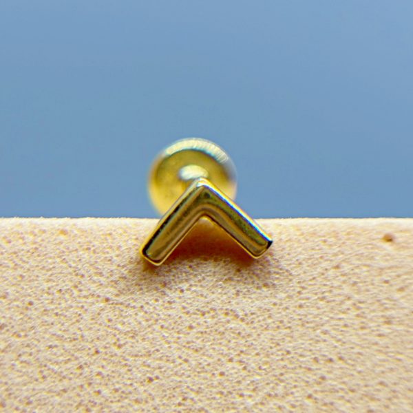 Close-up of a gold stud earring with a chevron-shaped front on a textured surface against a blue background