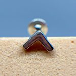 Close-up of a chrome chevron-shaped metal fitting against a blue background and speckled beige surface