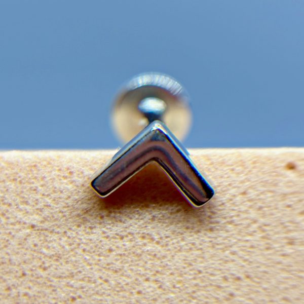 Close-up of a chrome chevron-shaped metal fitting against a blue background and speckled beige surface