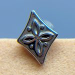 Close-up of a metallic diamond-shaped stud with a decorative floral pattern against a blue background